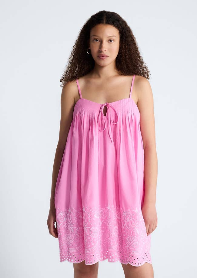 Person in a sleeveless, loose-fitting dress with a decorative hem, posing against a plain background