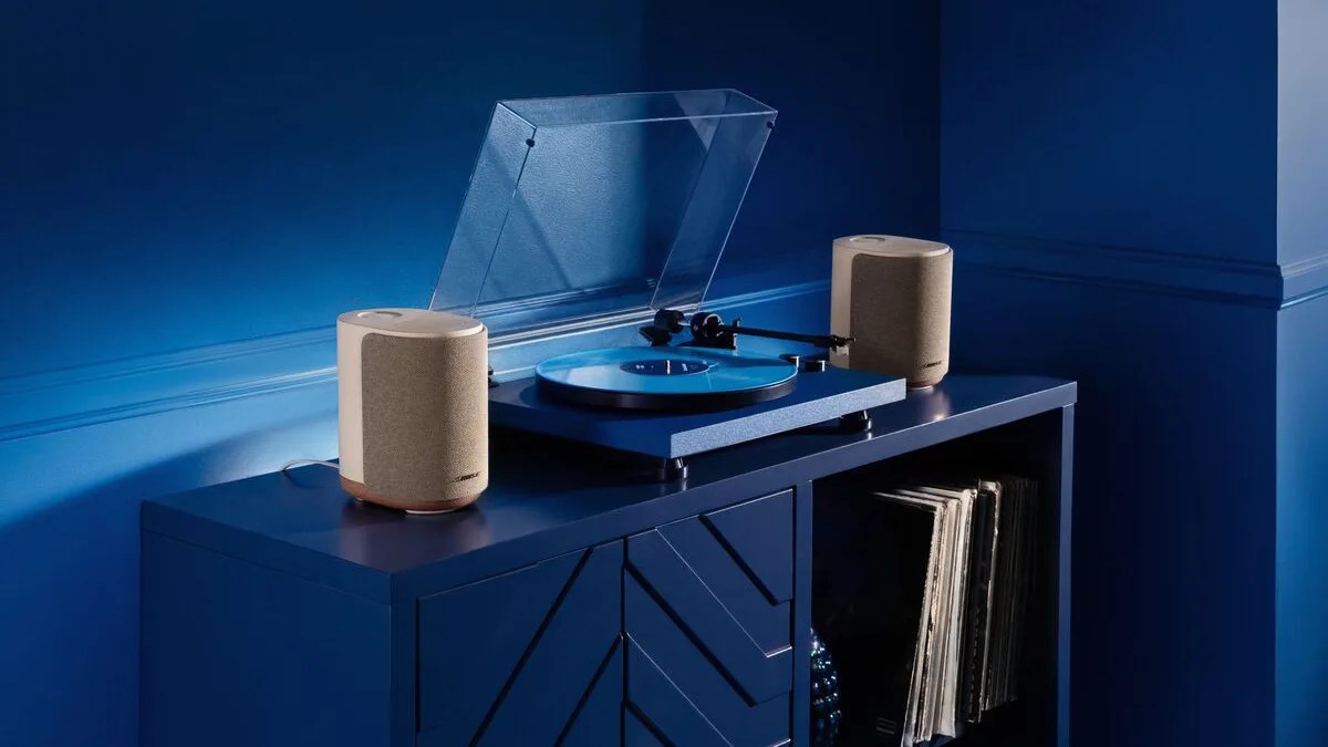 Blue turntable with a clear dust cover and two beige Bose speakers on a blue cabinet with vinyl records.