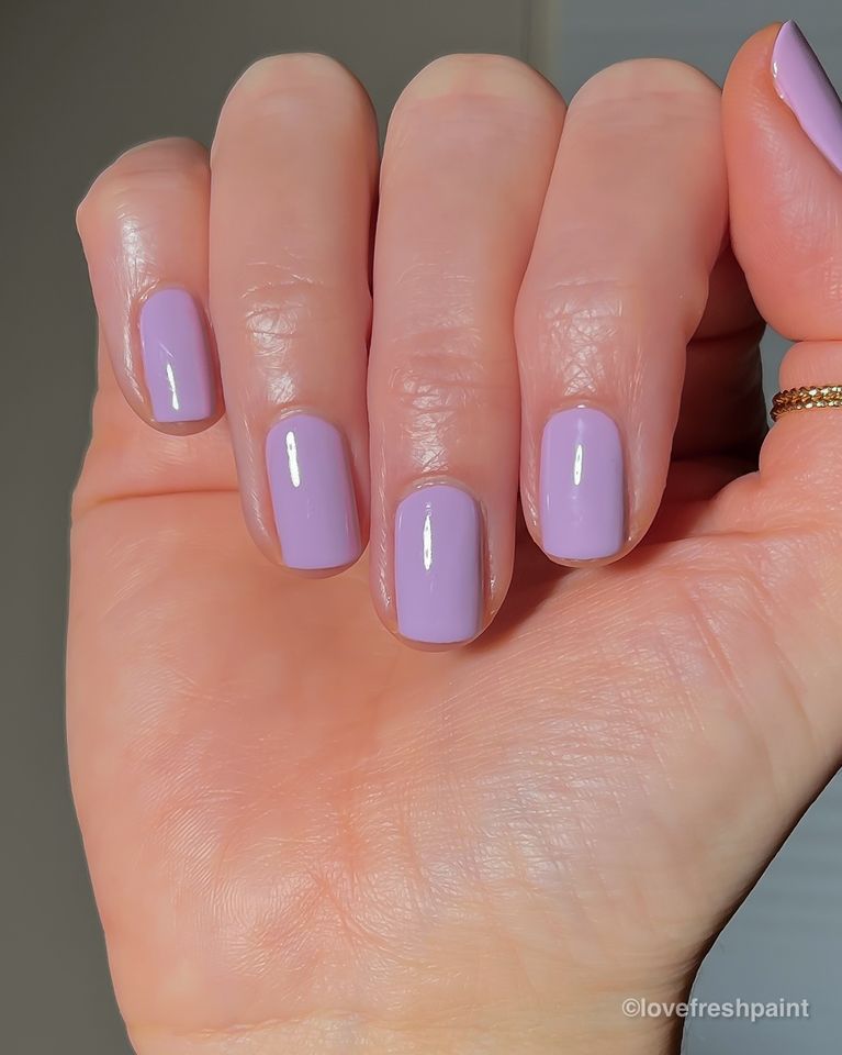A hand with neatly manicured nails painted in a light purple shade wearing a small ring on one finger
