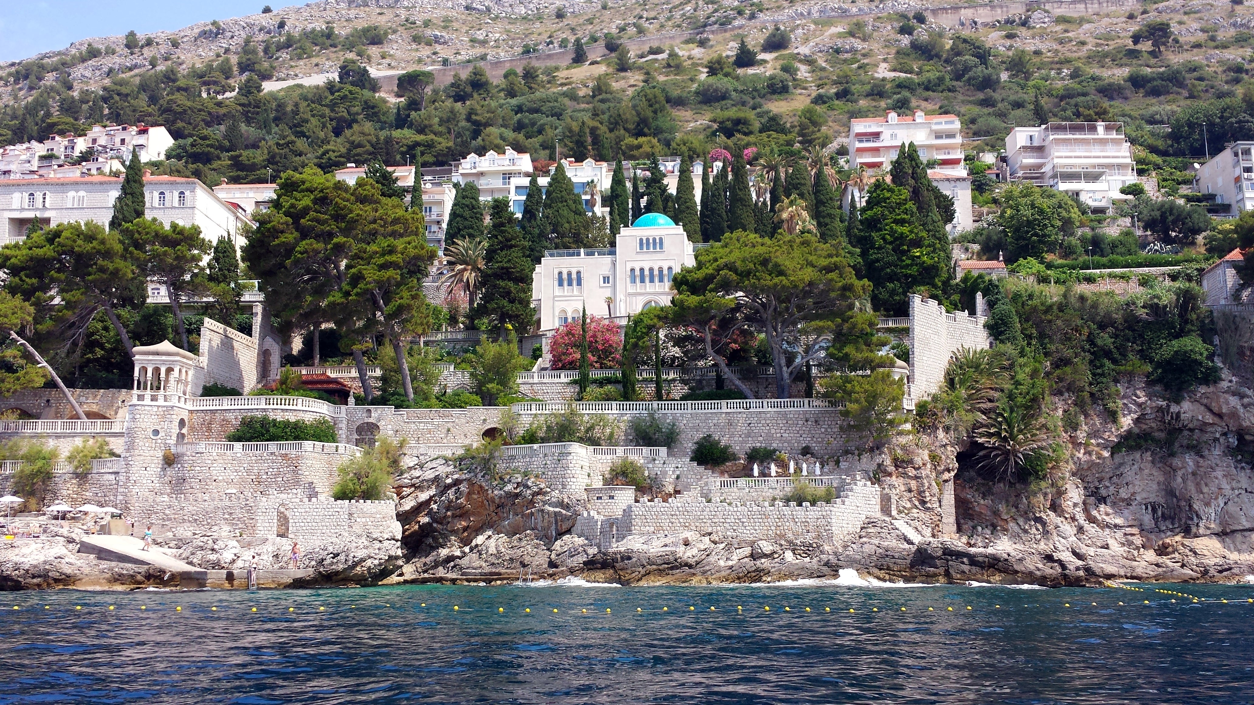 Scenic coastal view of Dubrovnik, Croatia, featuring historic architecture nestled among greenery on a hillside above the Adriatic Sea