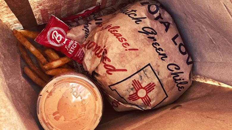Blake's Lotaburger paper bag with wrapped burgers, fries, and a side of sauce.