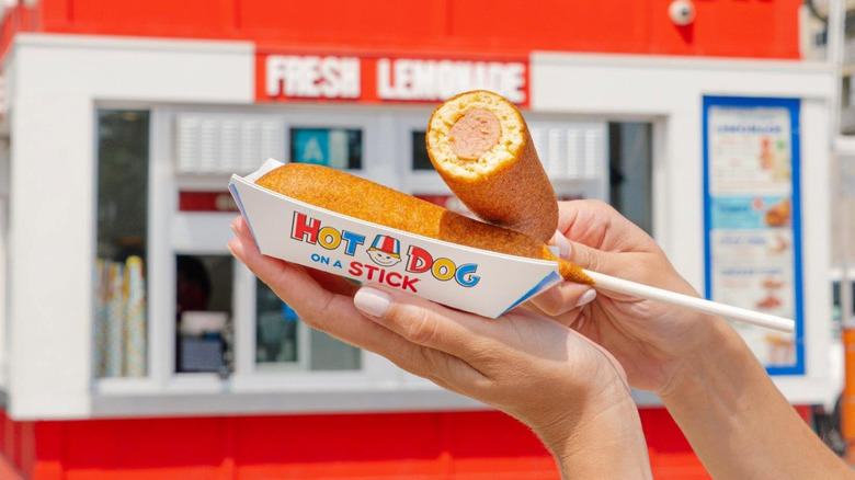 Hands holding fresh corn dogs from Hot Dog on a Stick