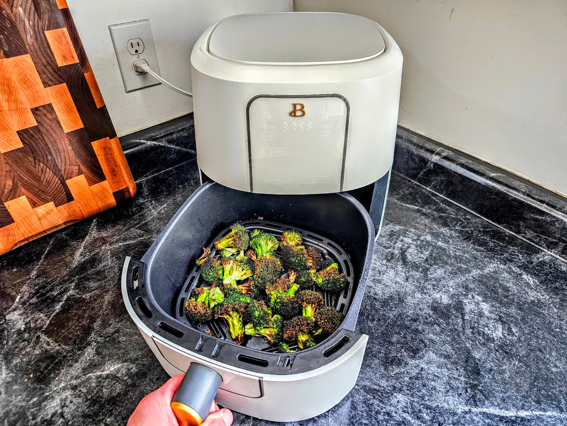 The Beautiful air fryer is displayed on a kitchen counter with broccoli in it.