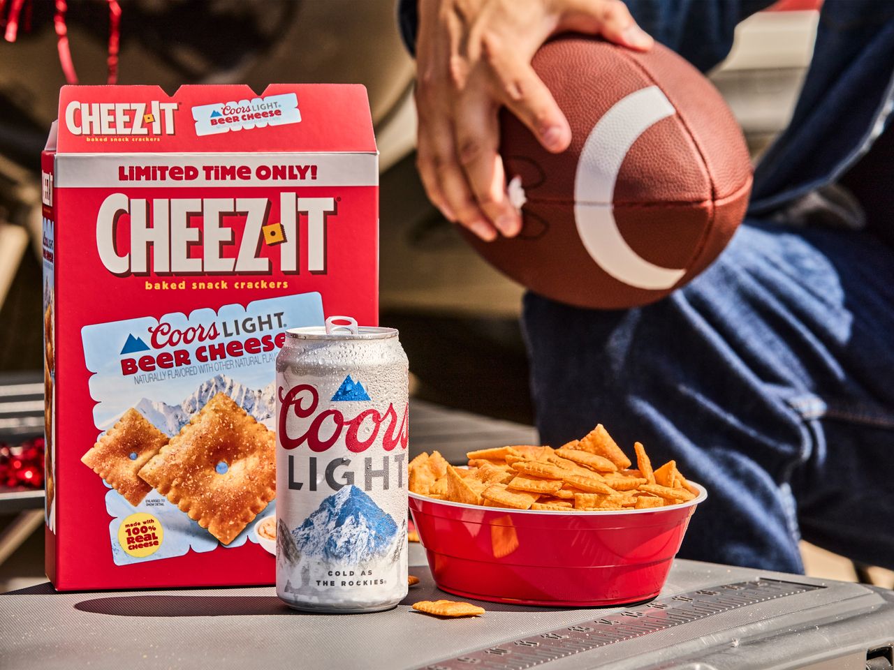 CheezIt box Coors Light can bowl of snacks and a person holding a football