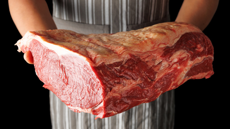 an aproned person holding a large sirloin roast with a fat cap on top