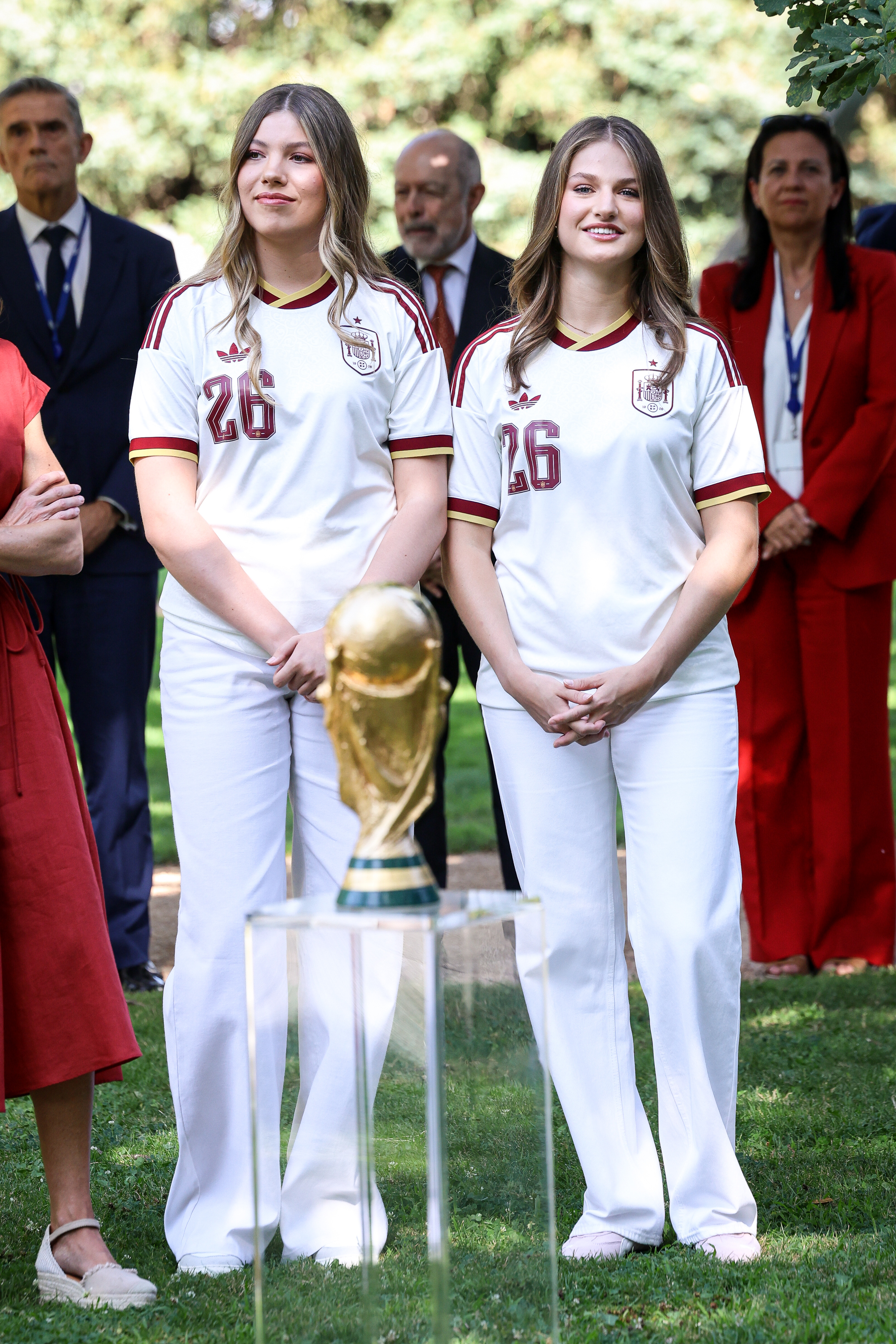 Princess Leonor and Infanta Sofia posing in soccer jerseys with the World Cup trophy