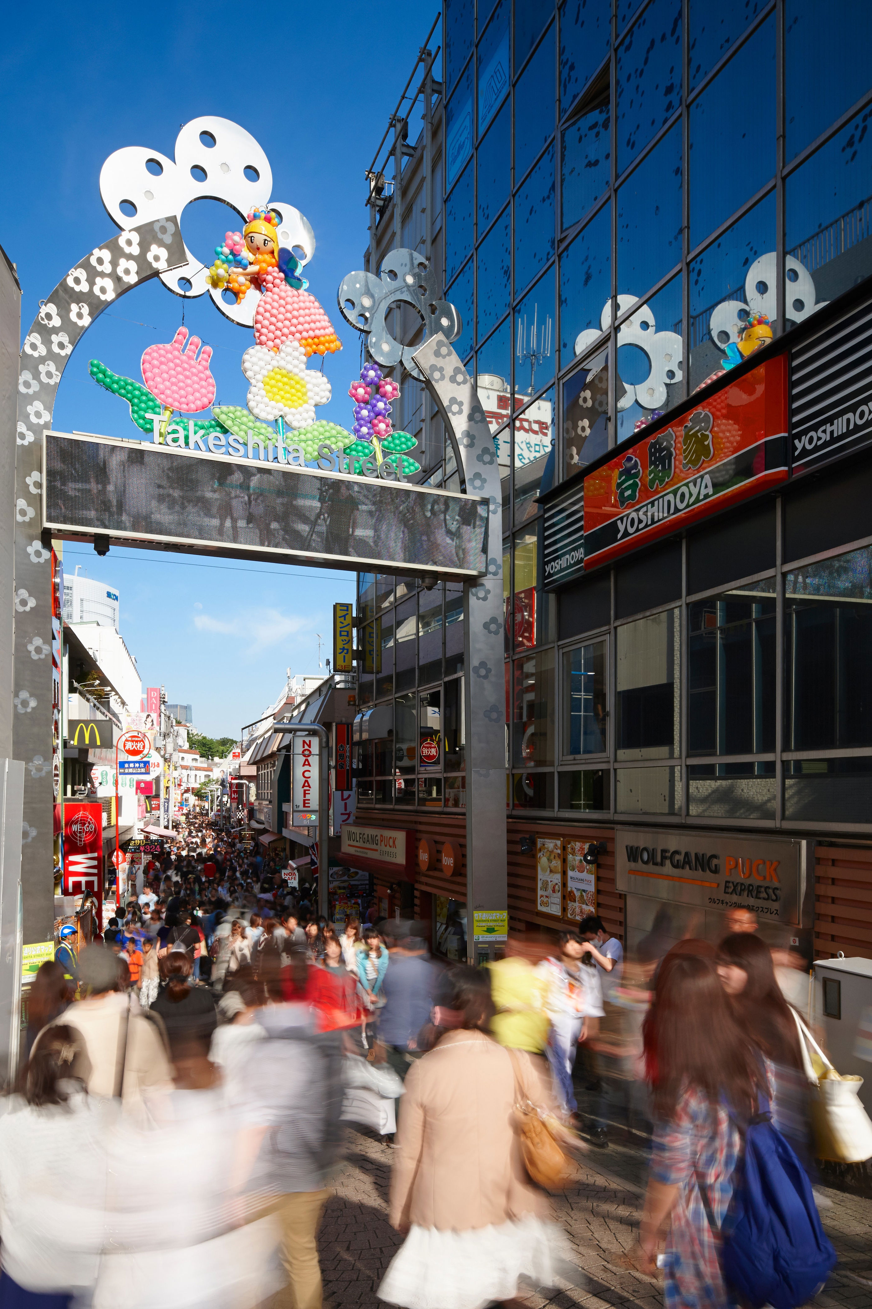 Bustling Takeshita Street in Tokyo, Japan, with people walking under a decorative archway between shops and eateries