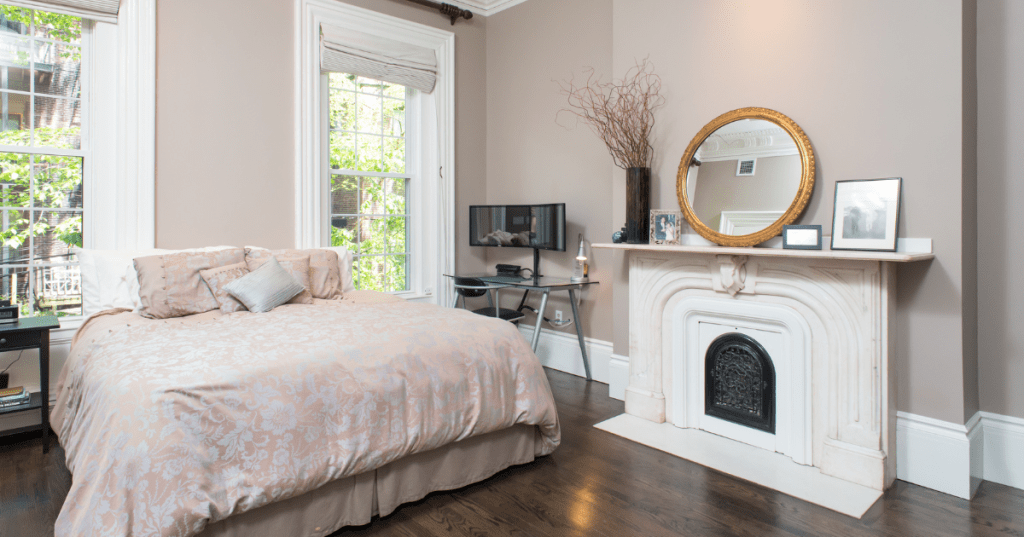 The interior of an Airbnb in Boston, Massachusetts, with a big bed in front of two windows and a marble fireplace.