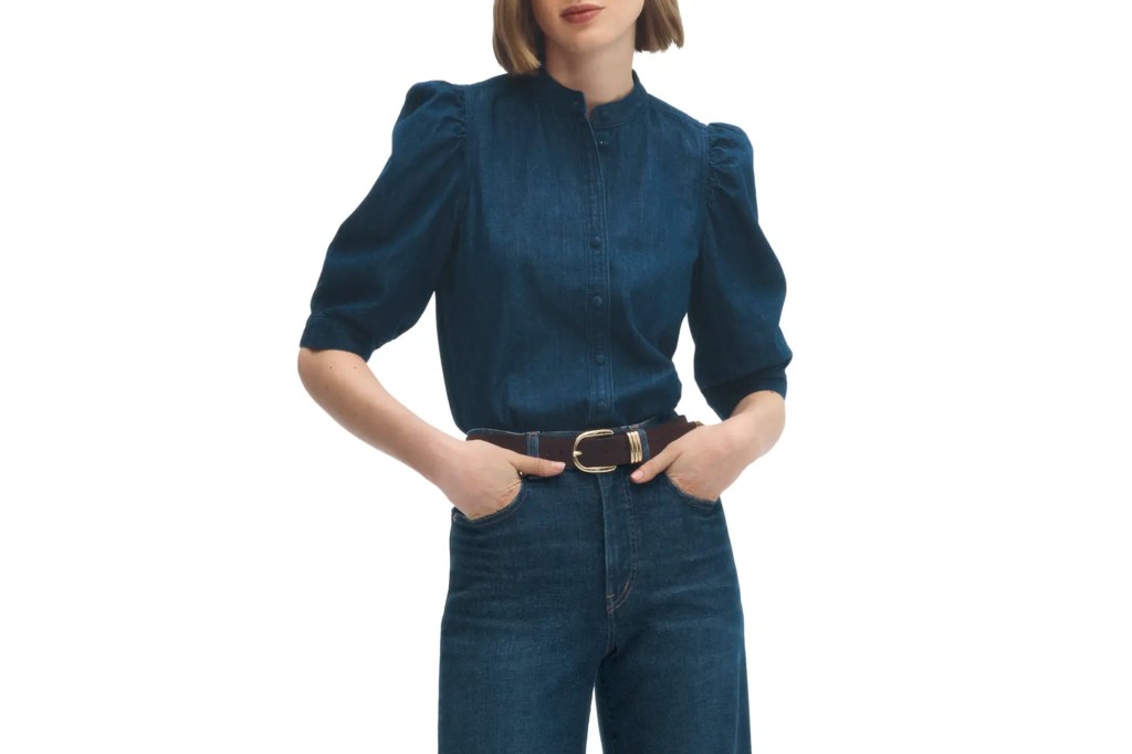 A woman in a dark blue denim shirt with puffed sleeves and jeans, wearing a brown belt with a gold buckle.