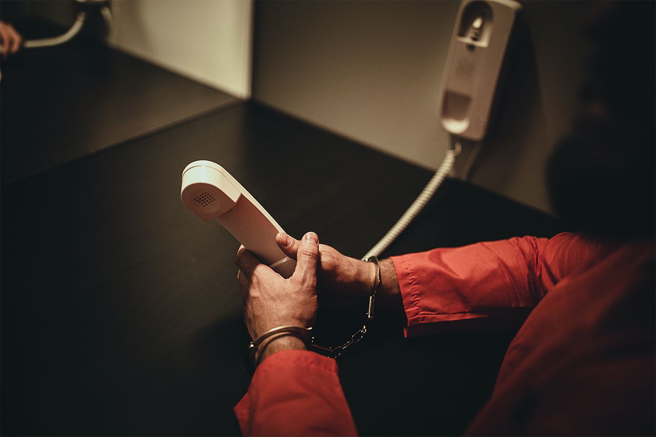 Stock photo of a male prisoner holding phone in prison visit room.