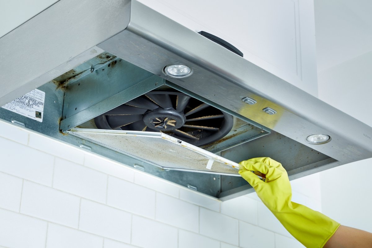 A gloved hand is cleaning a range hood.