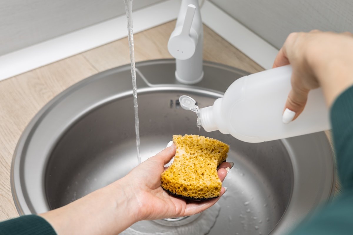 A person uses rubbing alcohol to disinfect a dish sponge.