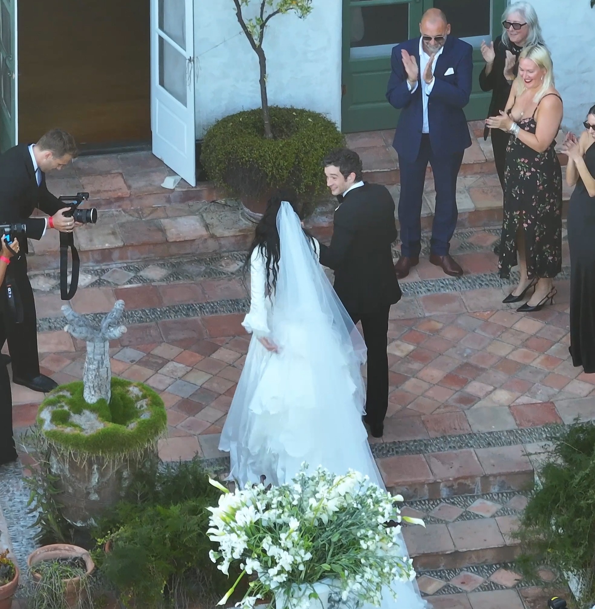 Matty Healy and Gabbriette Bechtel at their wedding, with guests applauding in the background.