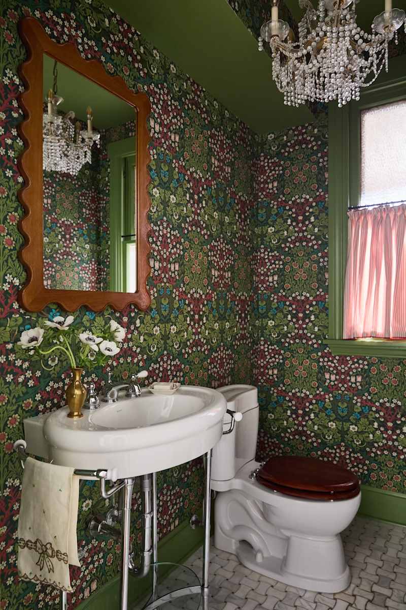 Vintage bathroom with floral wallpaper, a white sink, a wooden toilet seat, and a crystal chandelier.