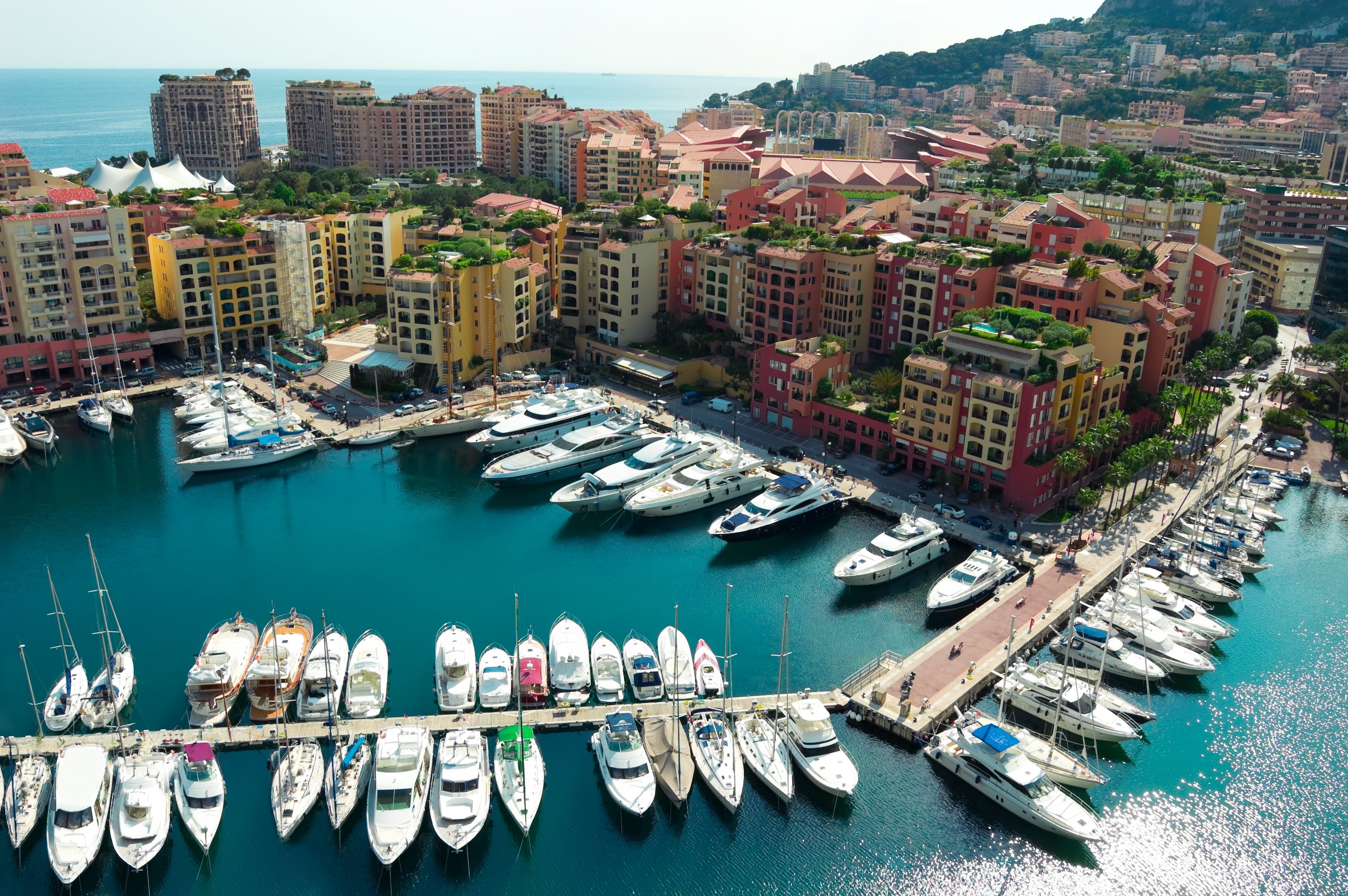 Aerial view of a marina with numerous yachts docked, surrounded by vibrant buildings and coastline, suggesting a travel destination