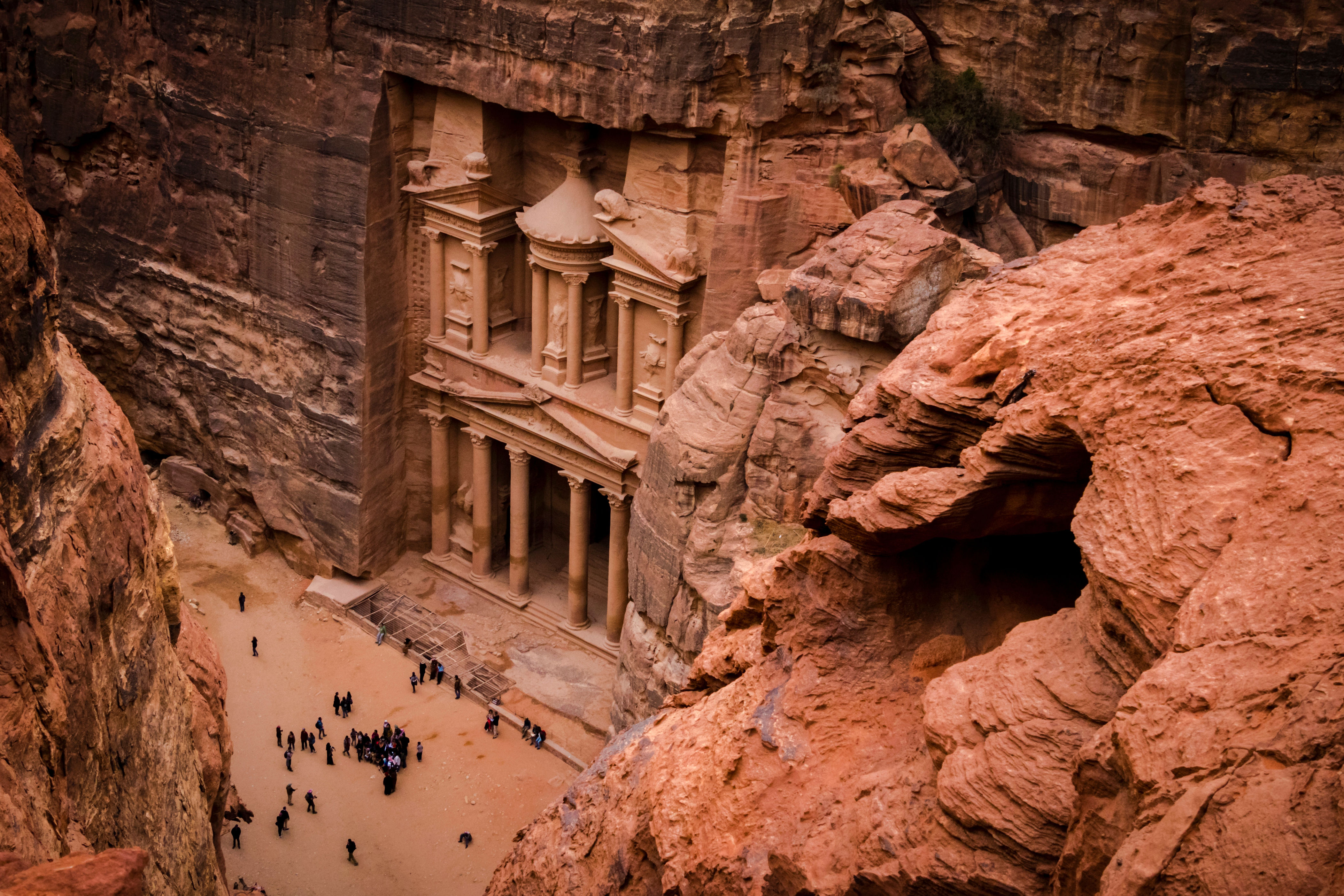 Ancient stone-carved Petra site in a desert landscape, with tourists exploring the area, showcasing its historic architecture
