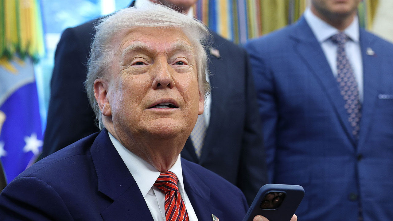 President Donald Trump holds a smartphone after signing executive orders in the Oval Office