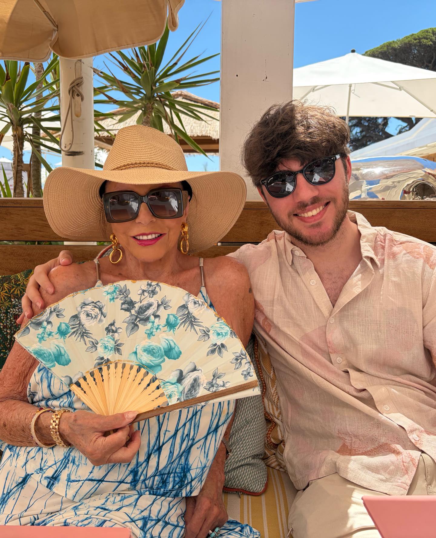 Joan Collins and Alison Papworth smiling together at a tropical outdoor setting.