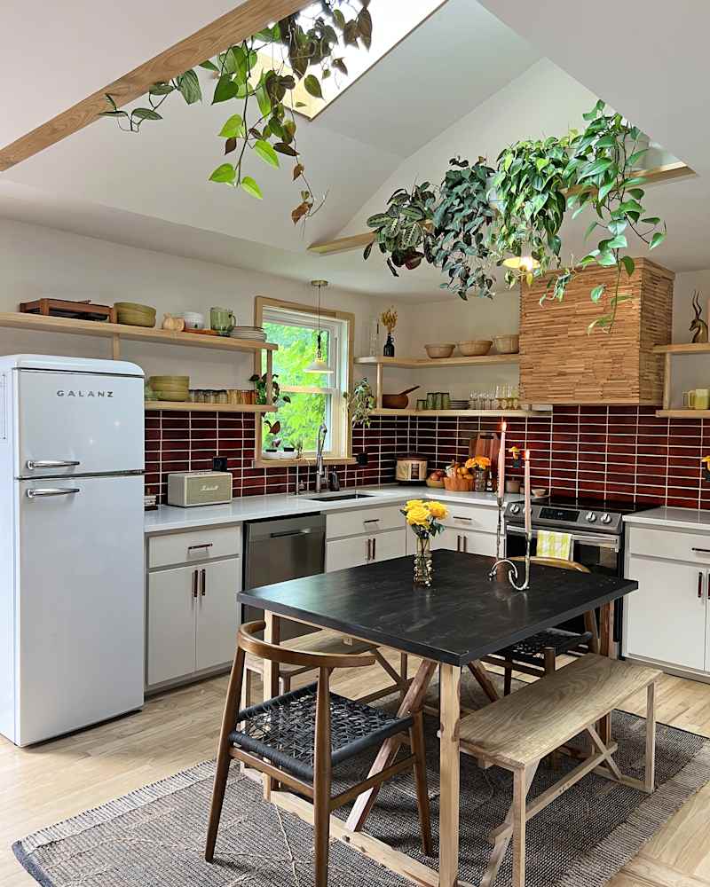 white kitchen with deep red tile backsplash and skylights with lots of plants
