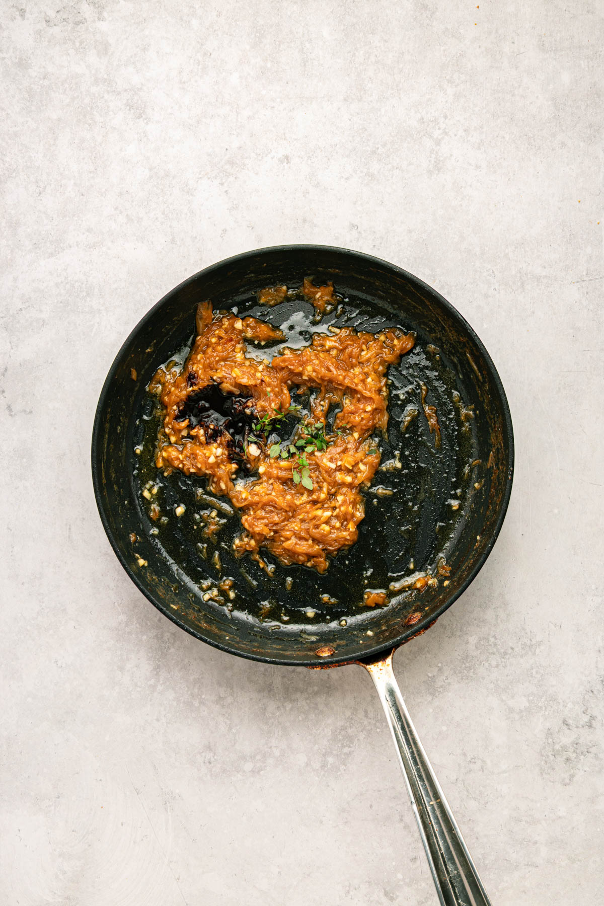 A black frying pan with a mixture of cooked onions, spices, and sauce, garnished with fresh herbs, sits on a light gray surface.