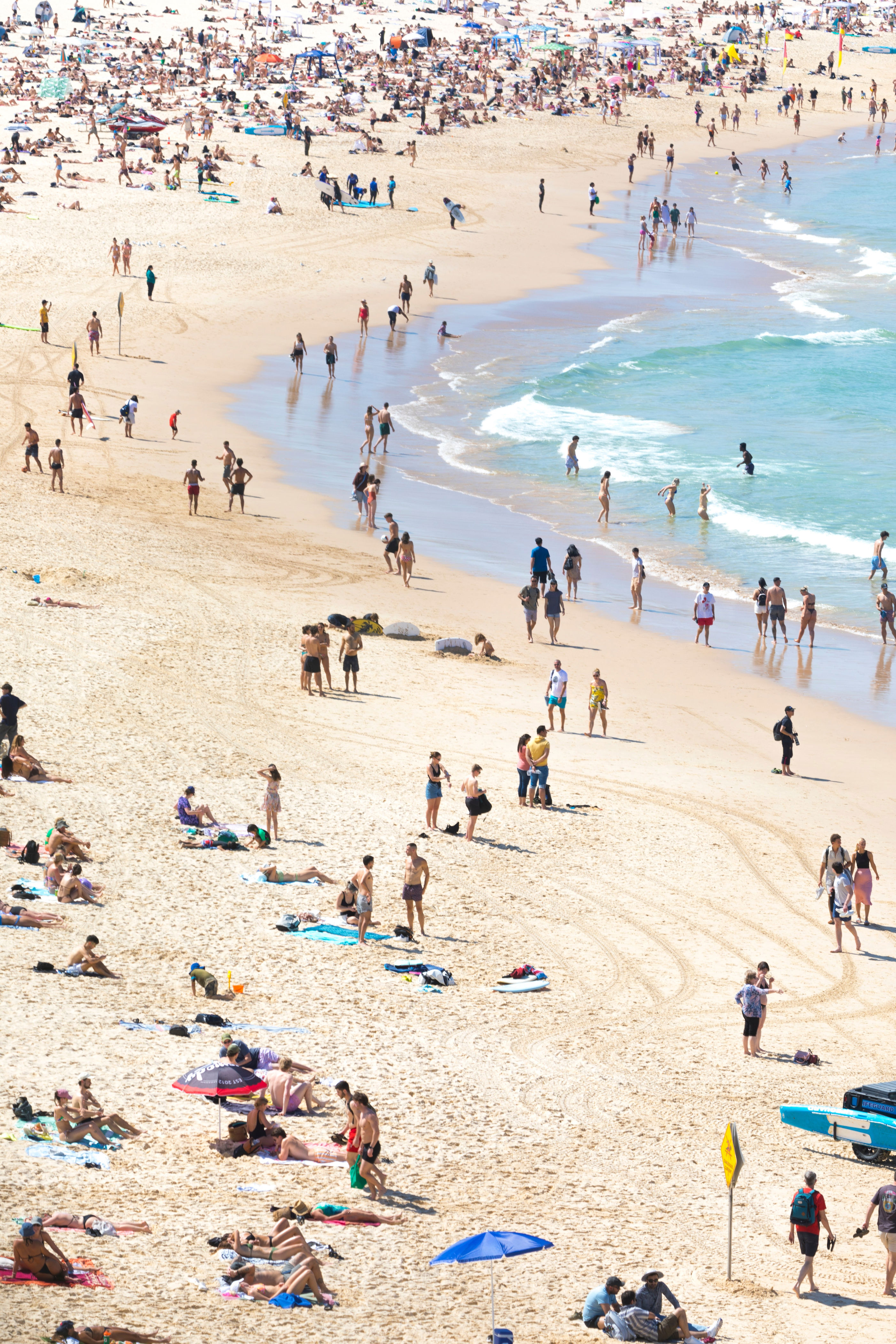 A crowded beach scene with people sunbathing and swimming in the ocean, highlighting a popular travel destination