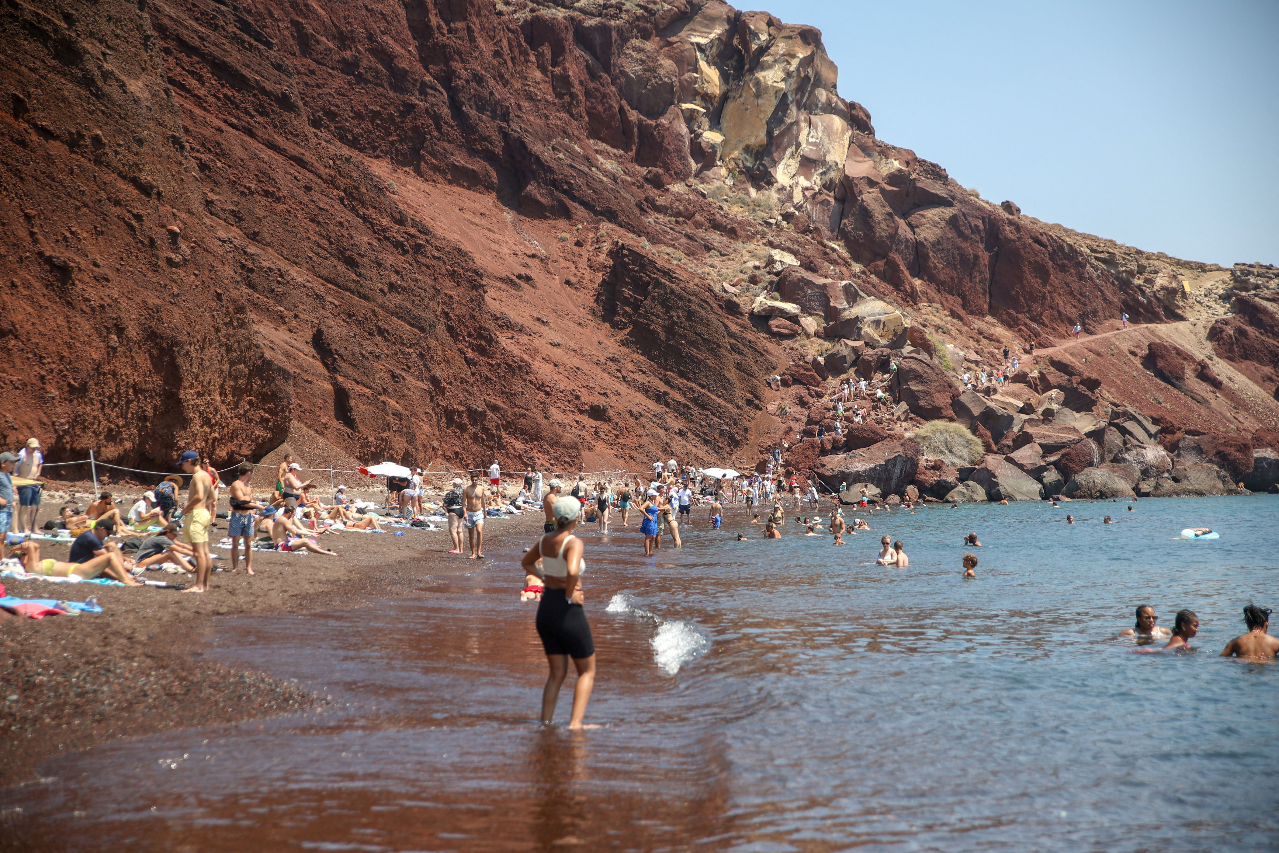 People enjoying a rocky beach with a cliff backdrop, swimming and sunbathing, exemplifying a popular travel destination