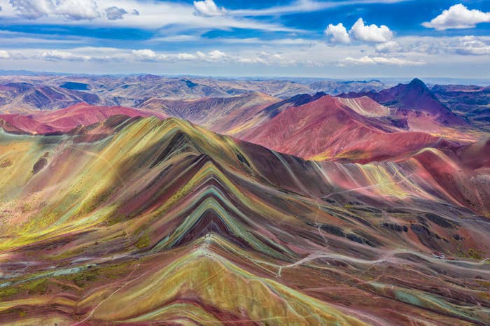Aerial view of the vibrant striped Rainbow Mountain range in Peru under a cloudy sky, known for its colorful mineral layers and scenic hiking trails