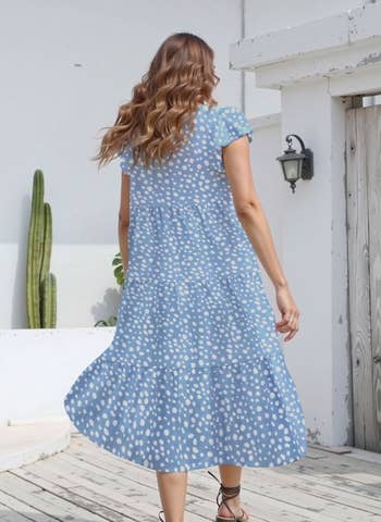 Person in a flowing, patterned dress walks on a wooden deck, cactus in background