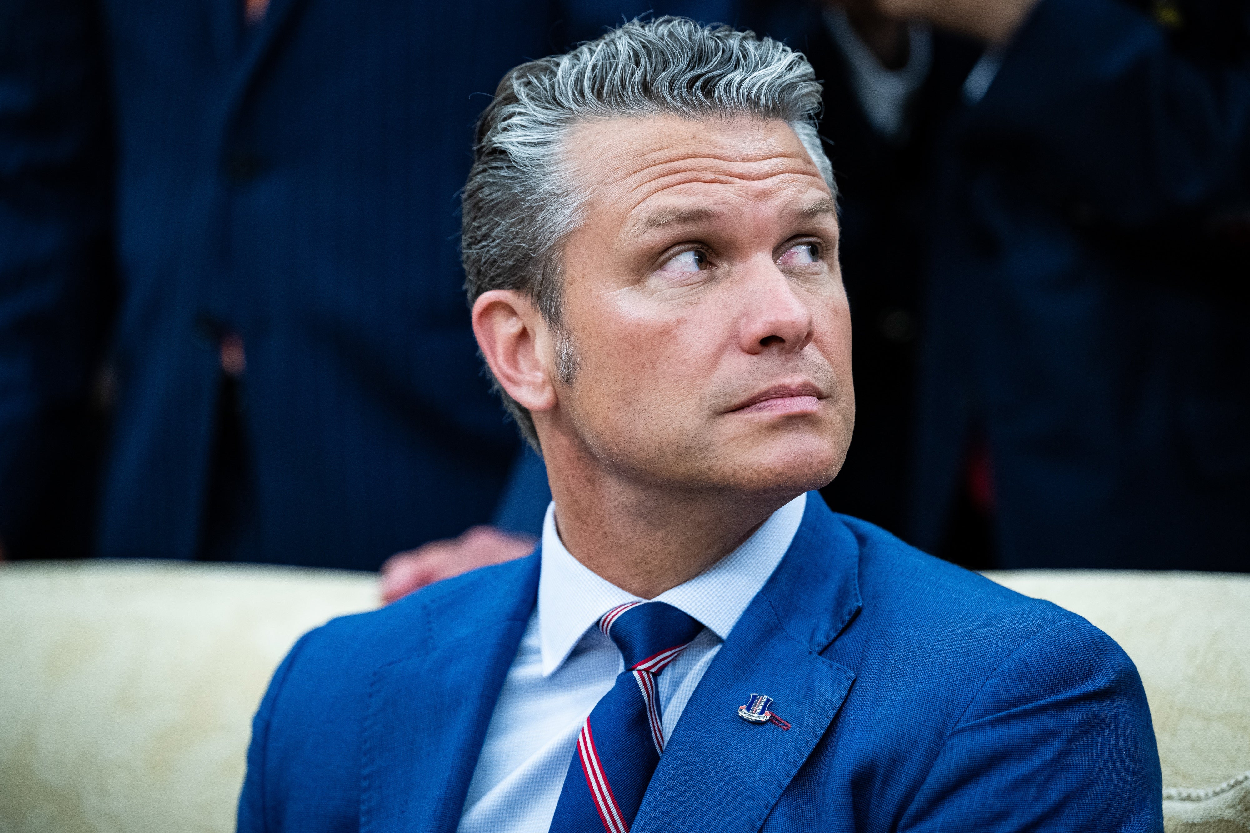 Man in a suit sitting indoors looking to the side, with a pensive expression