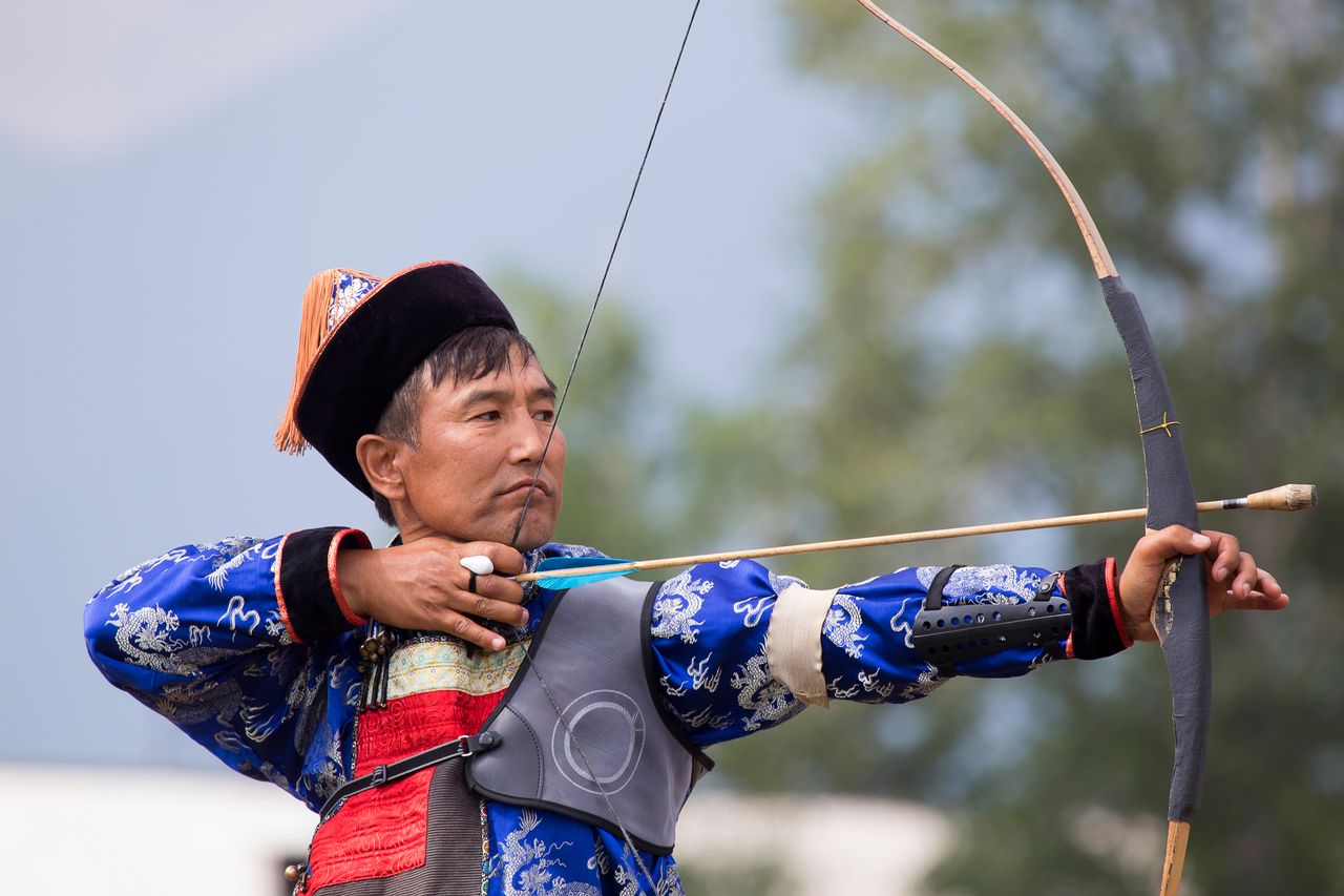 A man in traditional attire practicing archery with a bow and arrow