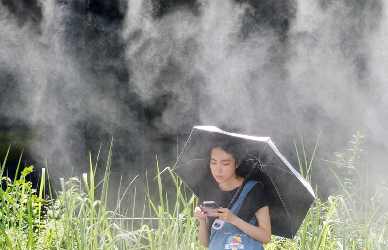 FILE PHOTO: A woman takes a break under a cooling mist during a heat wave in Tokyo