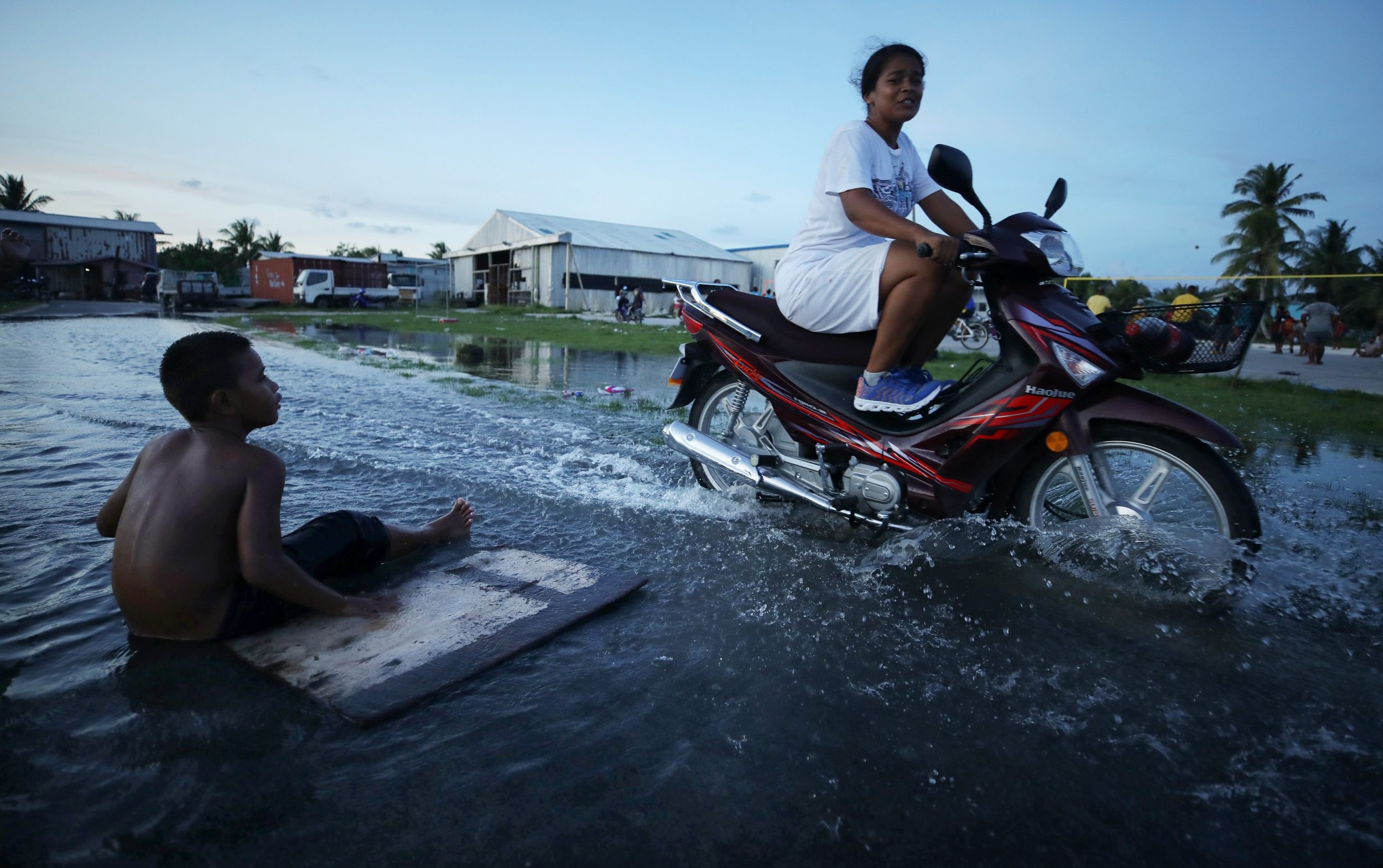 A woman rides her scooter through floodwaters occurring around high tide in a low lying area near the airport on November 27, 2019 in Funafuti, Tuvalu