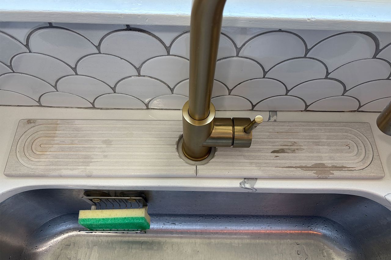 A kitchen sink faucet with a diatomite stone mat on the countertop a sponge visible in the basin