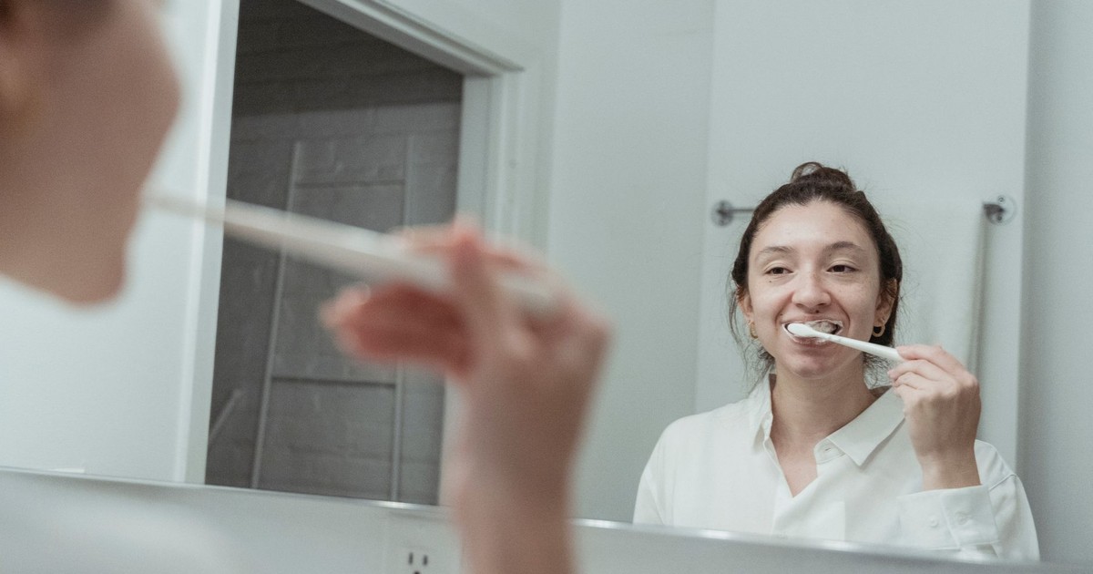 A woman with hair bun brushing her teeth in front of mirror, focusing on dental hygiene.