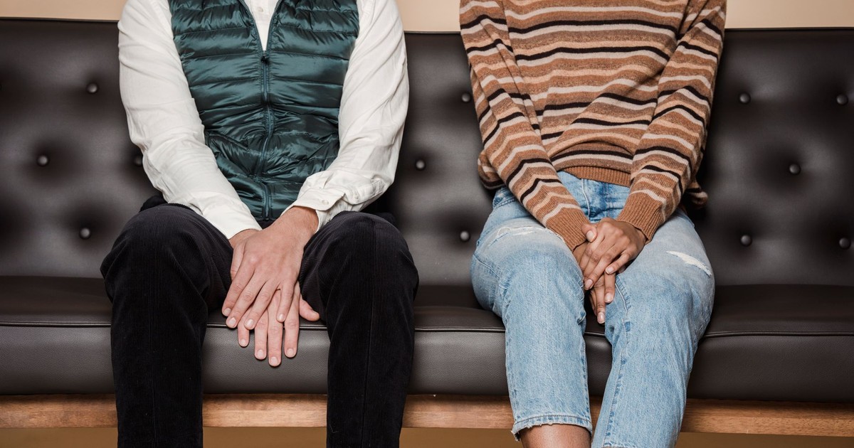 Unrecognizable couple in casual wear sitting on comfortable leather sofa in light living room at home while spending time together