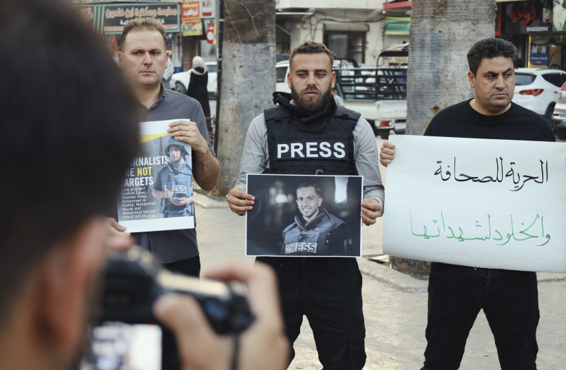 A man in a press vest holds a photo of a journalist beside protesters with signs in Arabic during a rally in Idlib, Syria on August 11, 2025. (credit: OMAR ALBAW/Middle East Images/AFP via Getty Images)