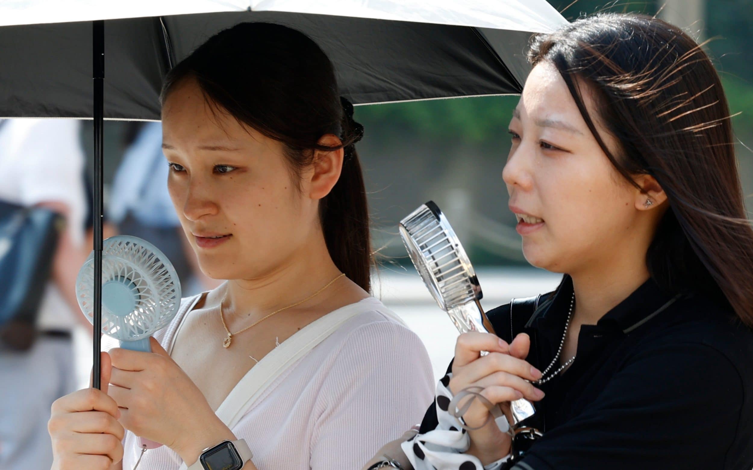 Women use electric fans and parasols to shield themselves from the sun amid high temperatures in Tokyo