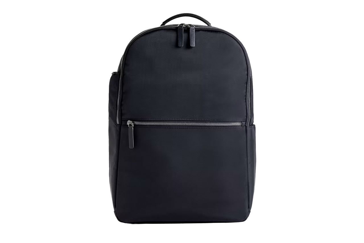 A slim travel backpack with a front zipper pocket and top handle