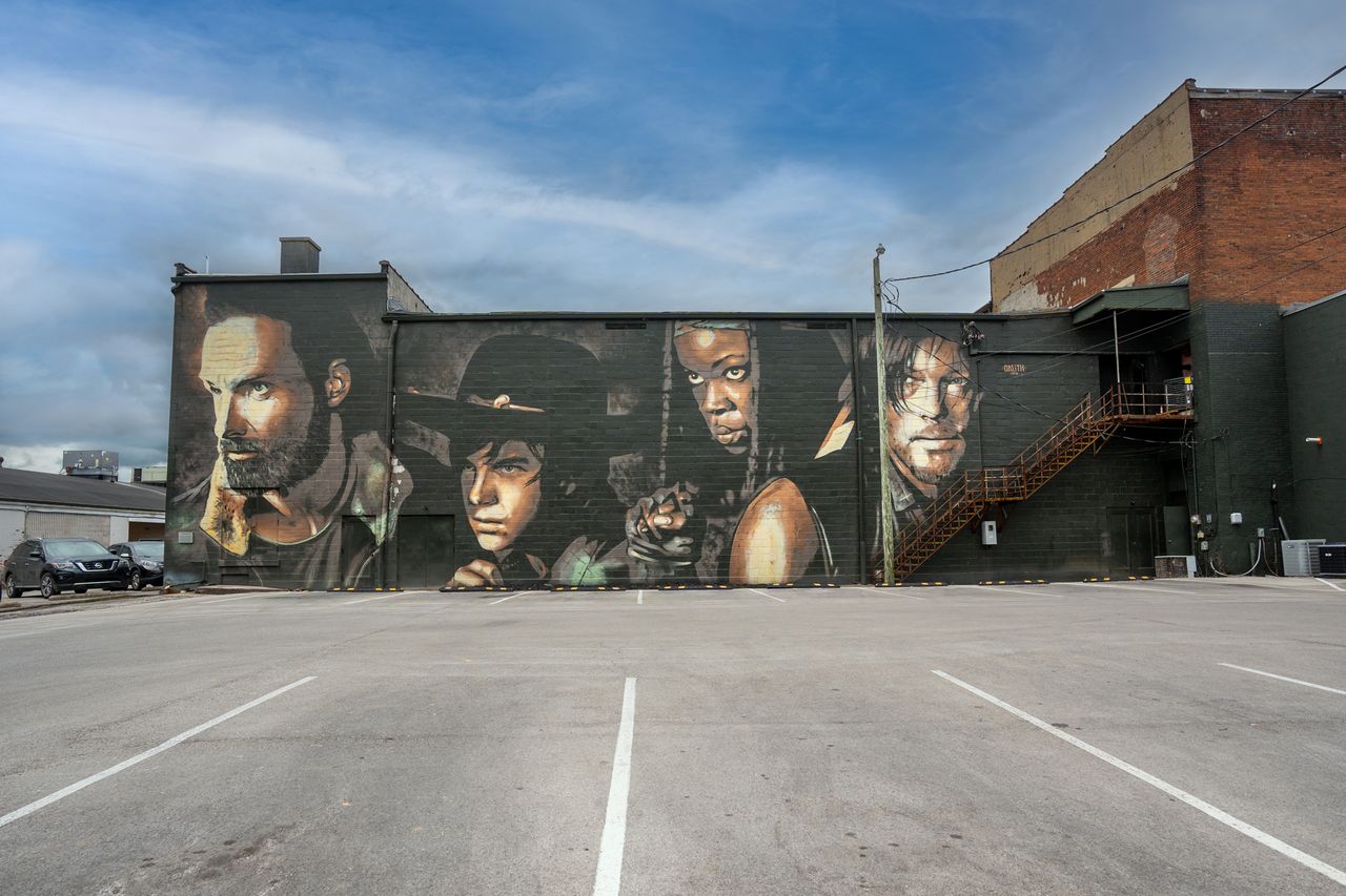 A mural featuring characters from a series including Norman Reedus displayed on a building wall in a parking lot