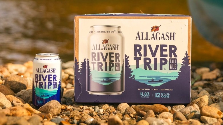 A can and case of Allagash River Trip Pale Ale on a rocky river bank