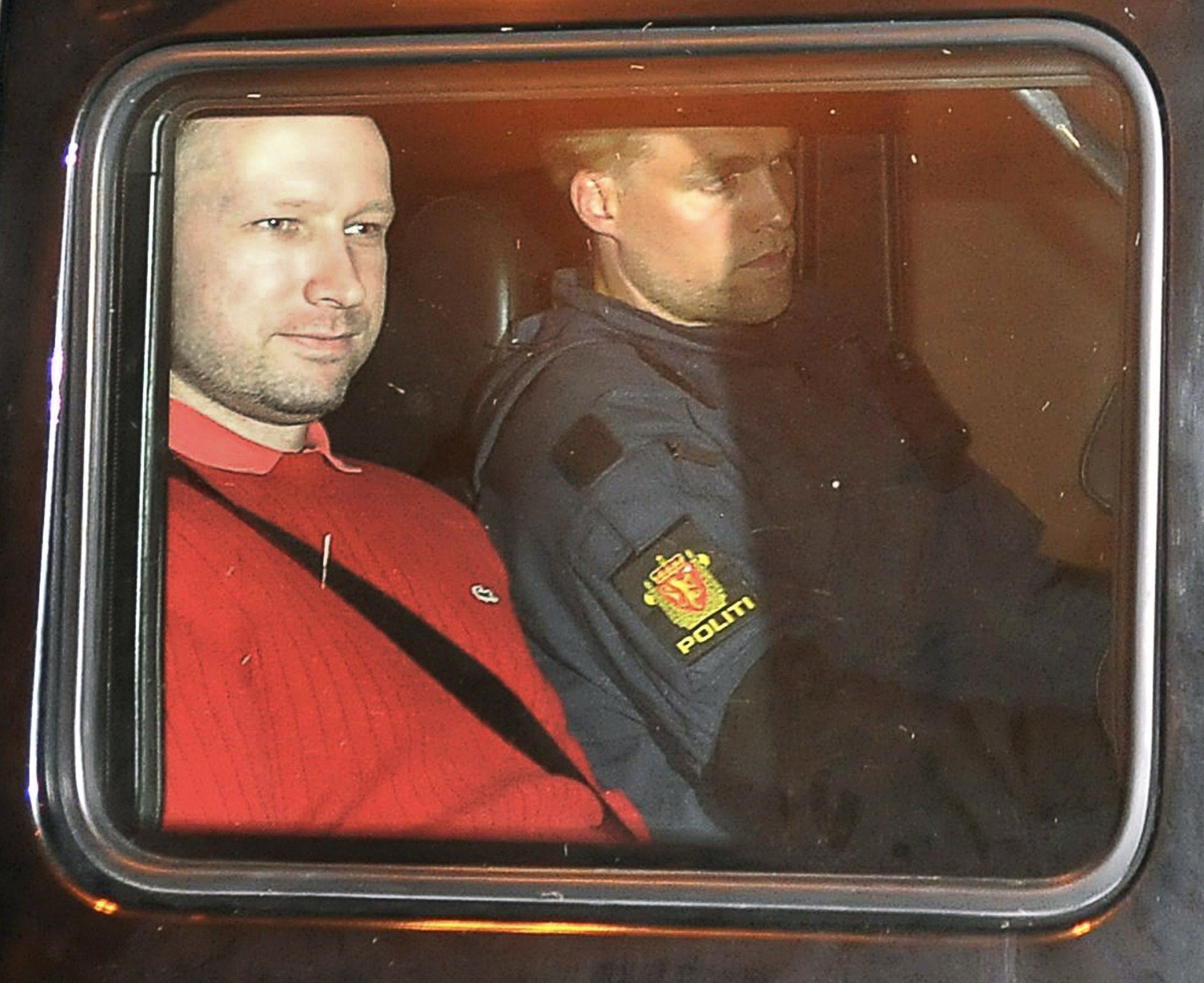 Bomb and terror suspect Anders Behring Breivik wearing a red top leaves the courthouse in a police car in Oslo. There is a police officer next to him.