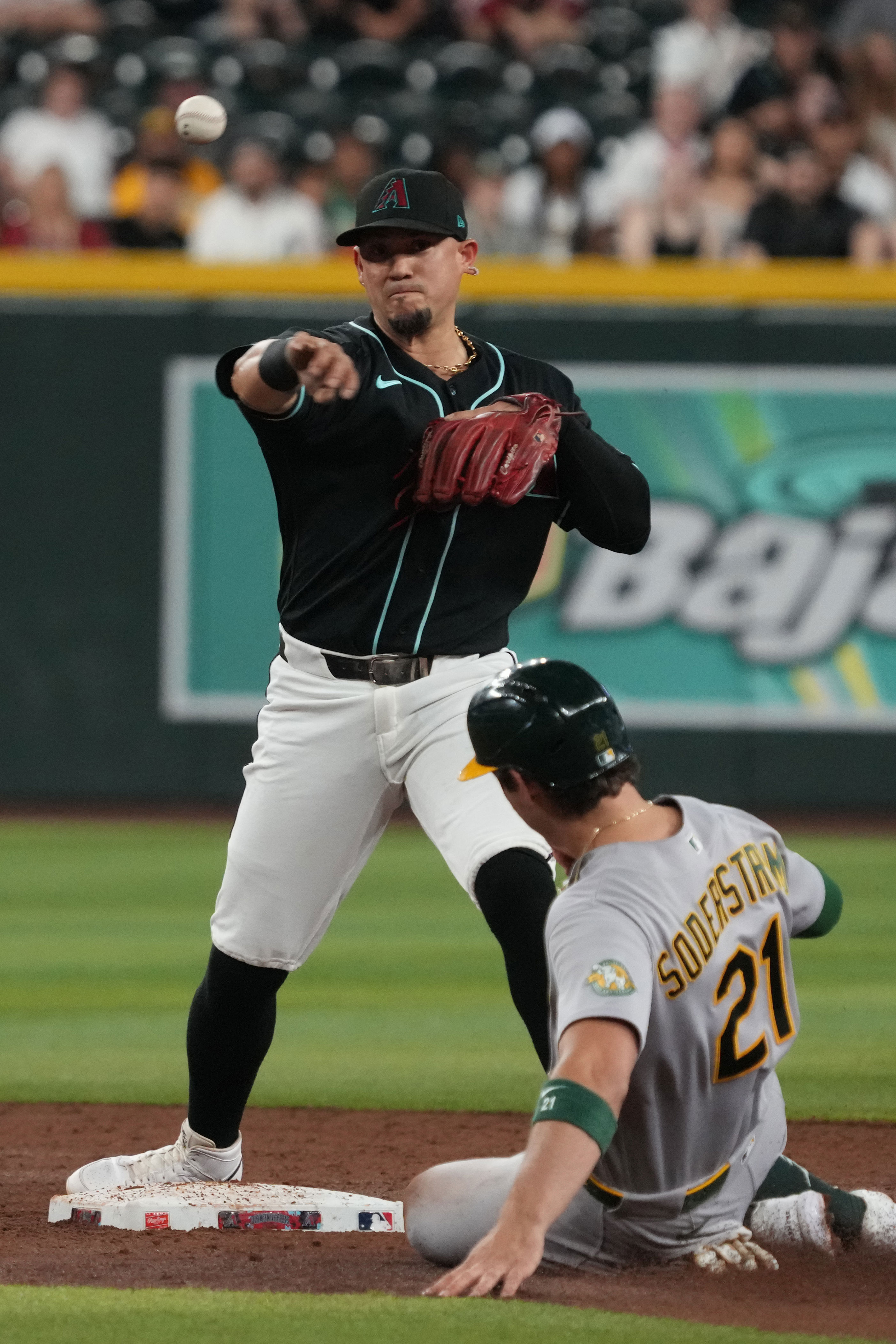 Arizona Diamondbacks second baseman Ildemaro Vargas turns the double play while avoiding Athletics' Tyler Soderstrom (21) on a ball hit by Jonah Heim in the third inning of a baseball game, Tuesday, July 21, 2026, in Phoenix. (AP Photo/Rick Scuteri)