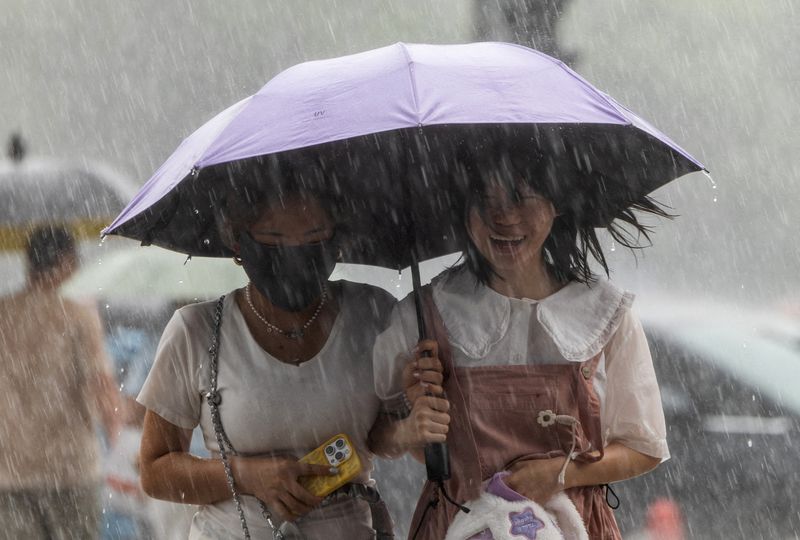 FILE PHOTO: Two women carrying an umbrella walk under heavy rain in Beijing