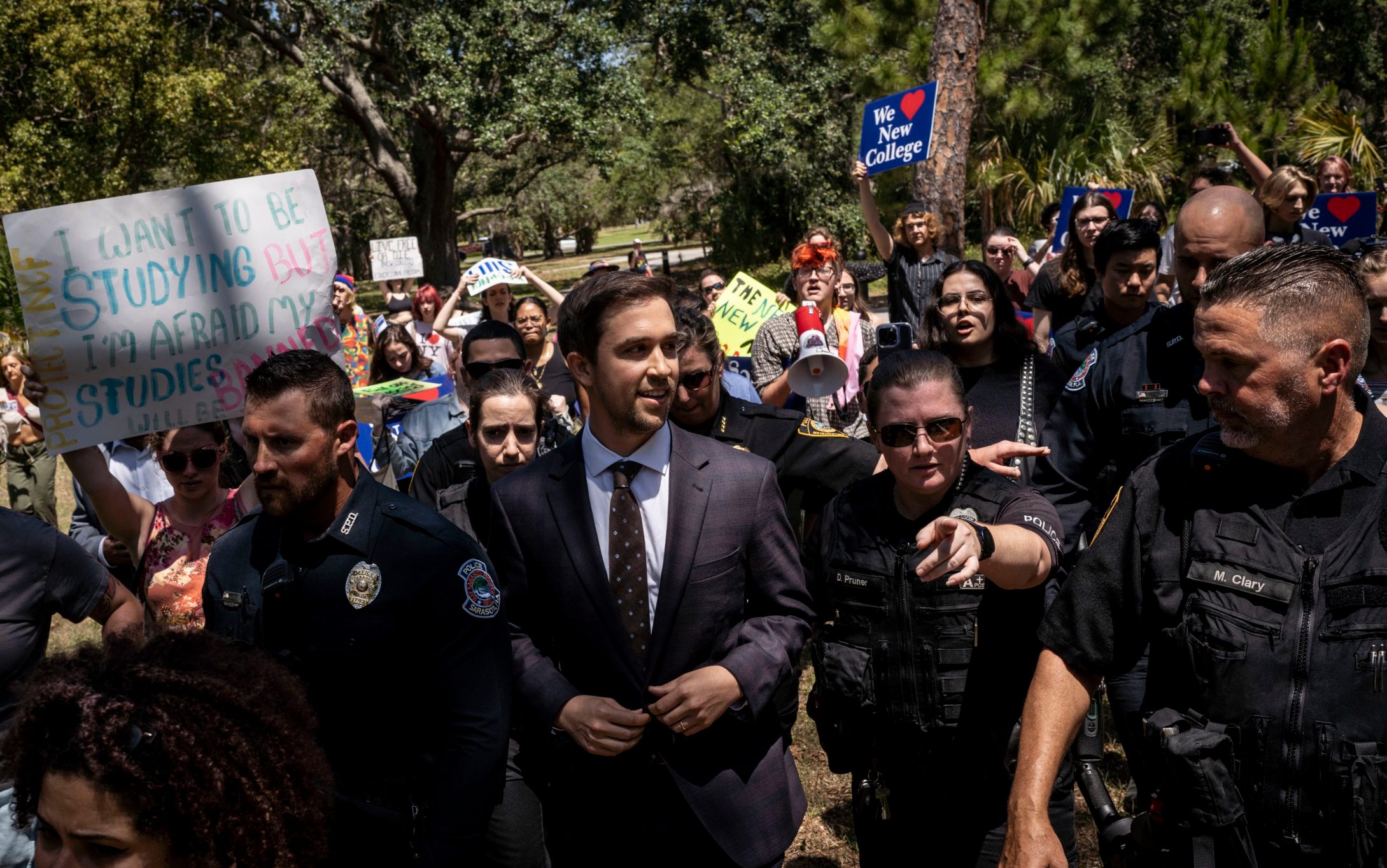 Christopher Rufo in a suit walking through a crowd of protesters in May 2023