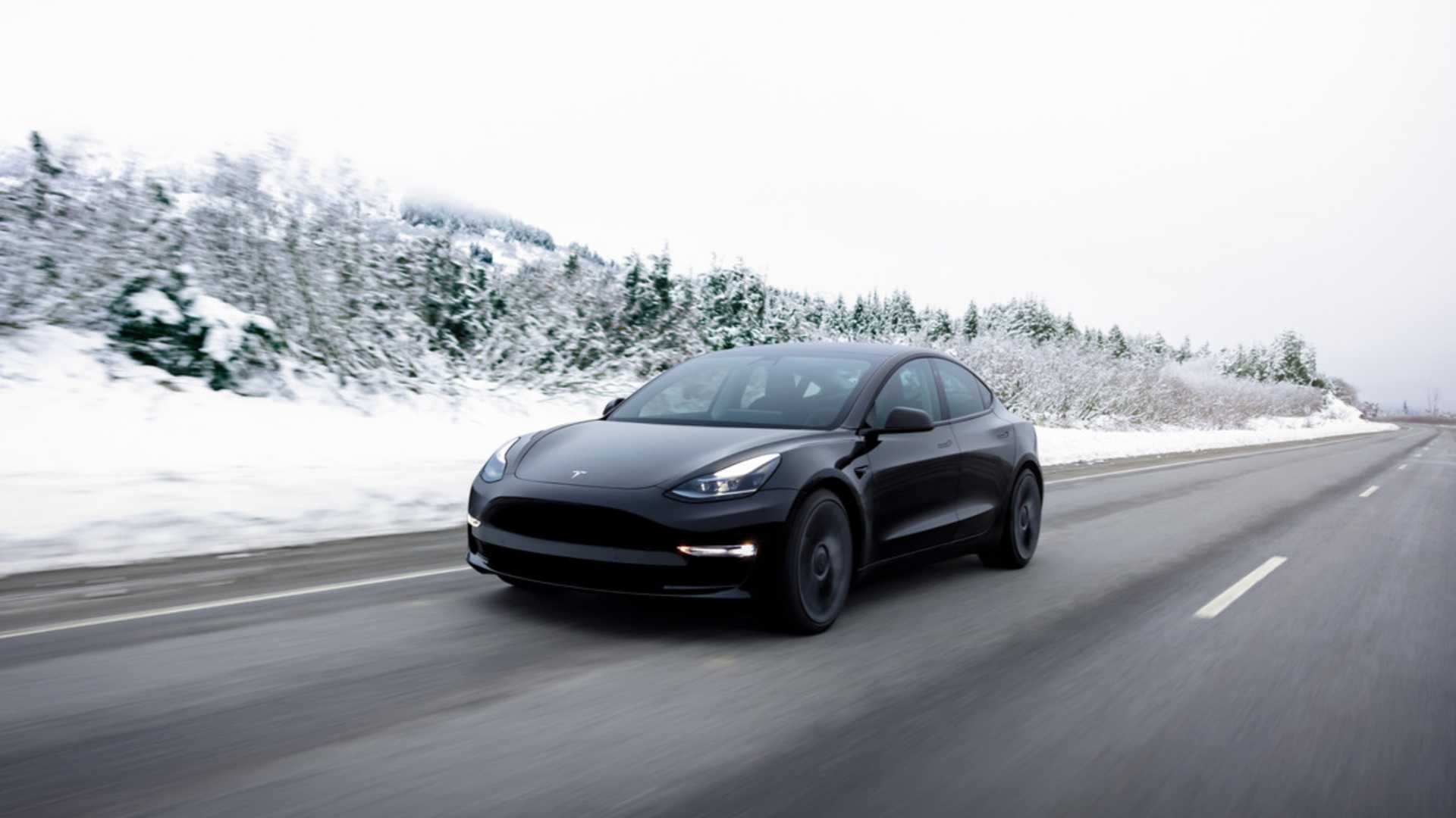 Three-quarter front view of black Tesla Model 3 driving on a highway