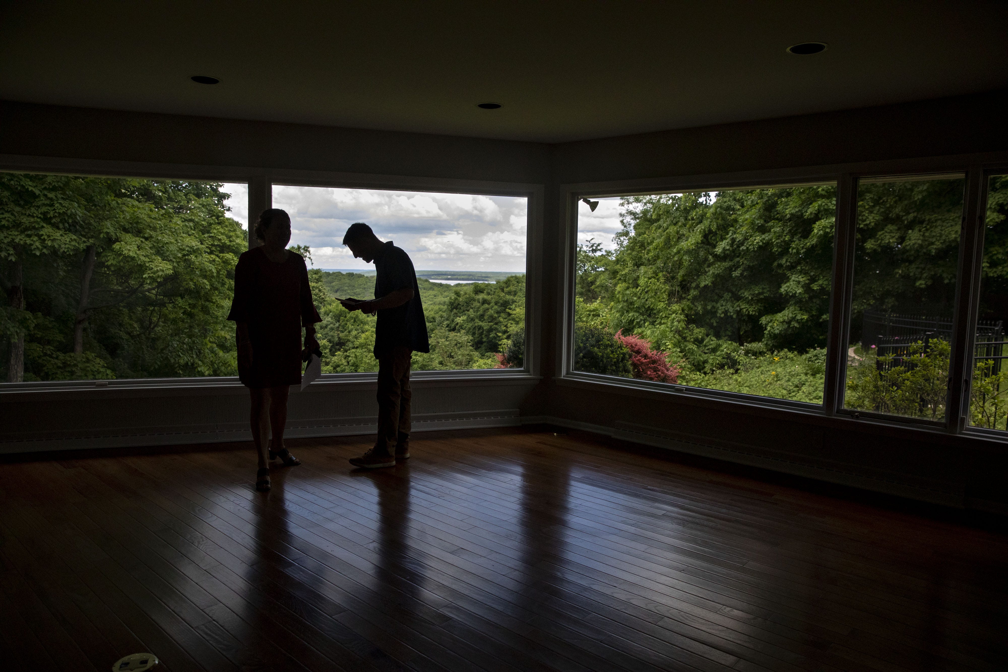 Silhouettes of two potential buyers against the window of an empty house during a tour.