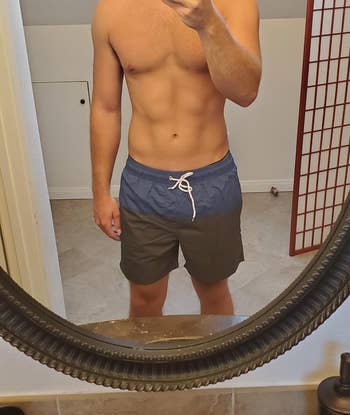 Person taking a mirror selfie, wearing two-tone swim trunks