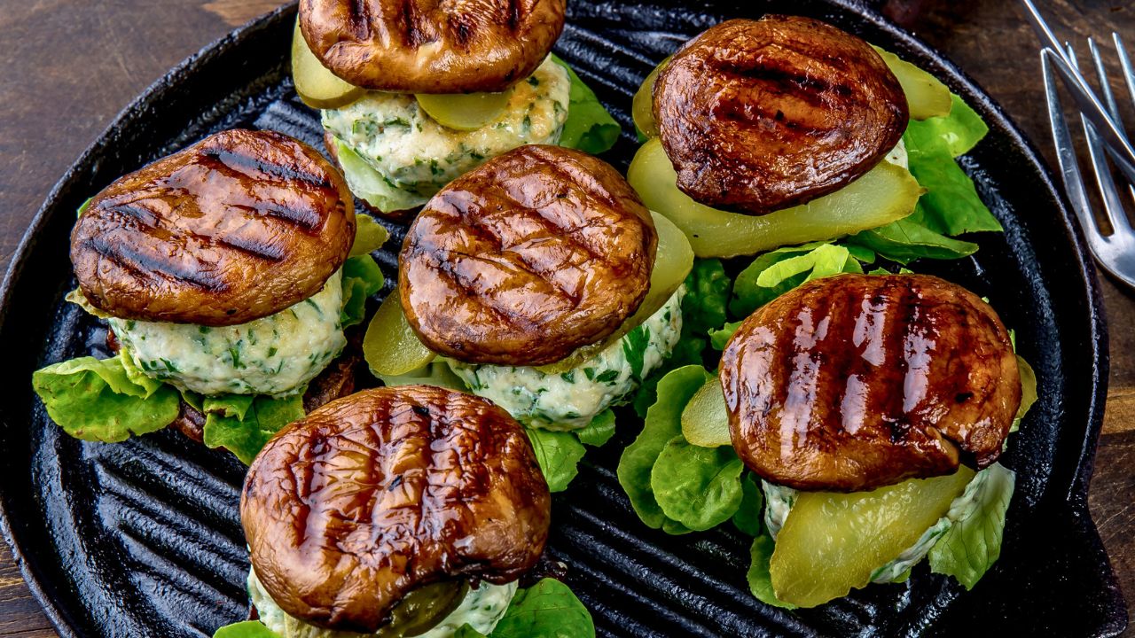 Six mushroom-topped appetizers on a black serving plate.