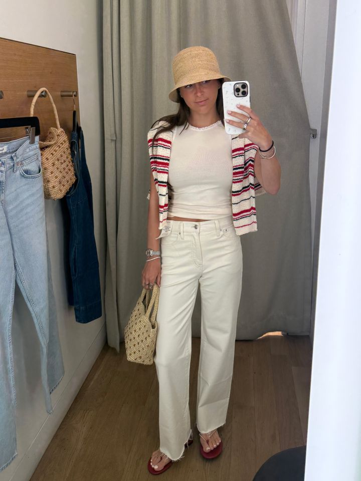 Person in a store trying on a summer outfit with a striped cardigan white trousers and a bucket hat taking a mirror selfie