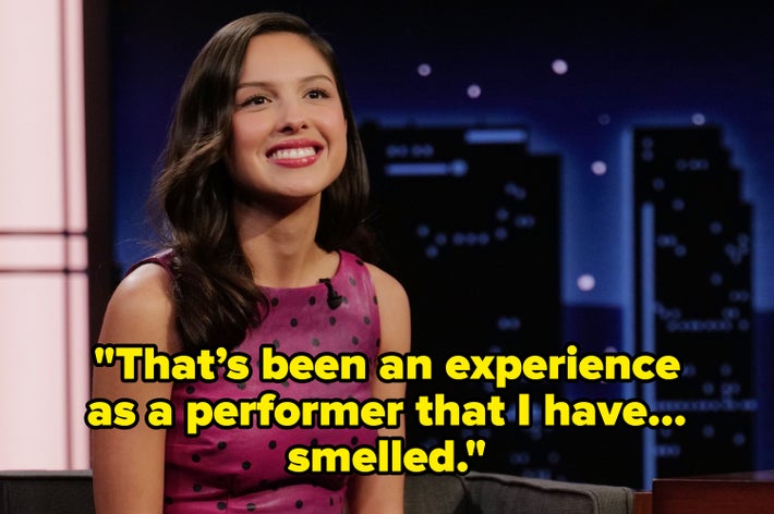 Person in a stylish, fitted dress with a polka dot pattern, sitting on a talk show set, smiling